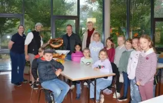 Gruppenfoto in der Mensa: Schülerinnen und Schüler mit Vertreterinnen und Vertretern von Schule, Gemeinde und „Bread and Brezel“, in der Mitte eine große Brezel und frische Backwaren