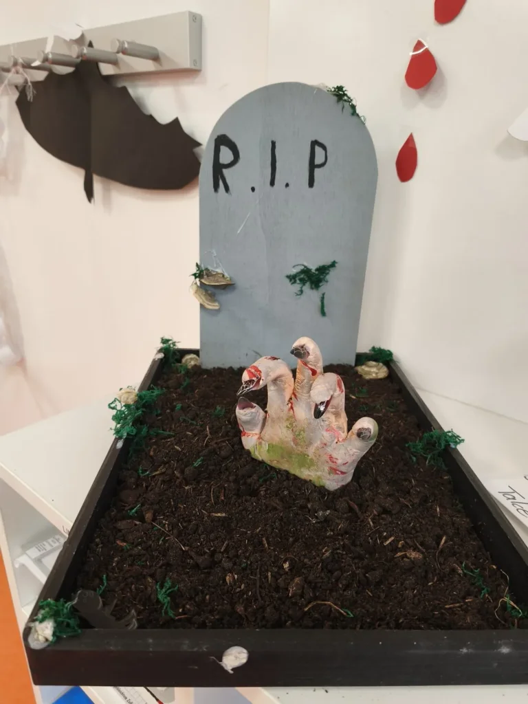 Grabstein mit der Aufschrift R.I.P. und einer Zombiehand, die aus der Erde ragt